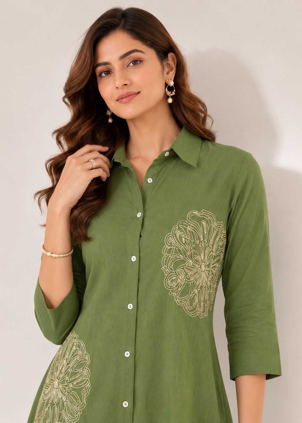 A woman wearing an olive green button-up shirt with beige floral embroidery on the chest and lower skirt, posed against a plain light beige background.