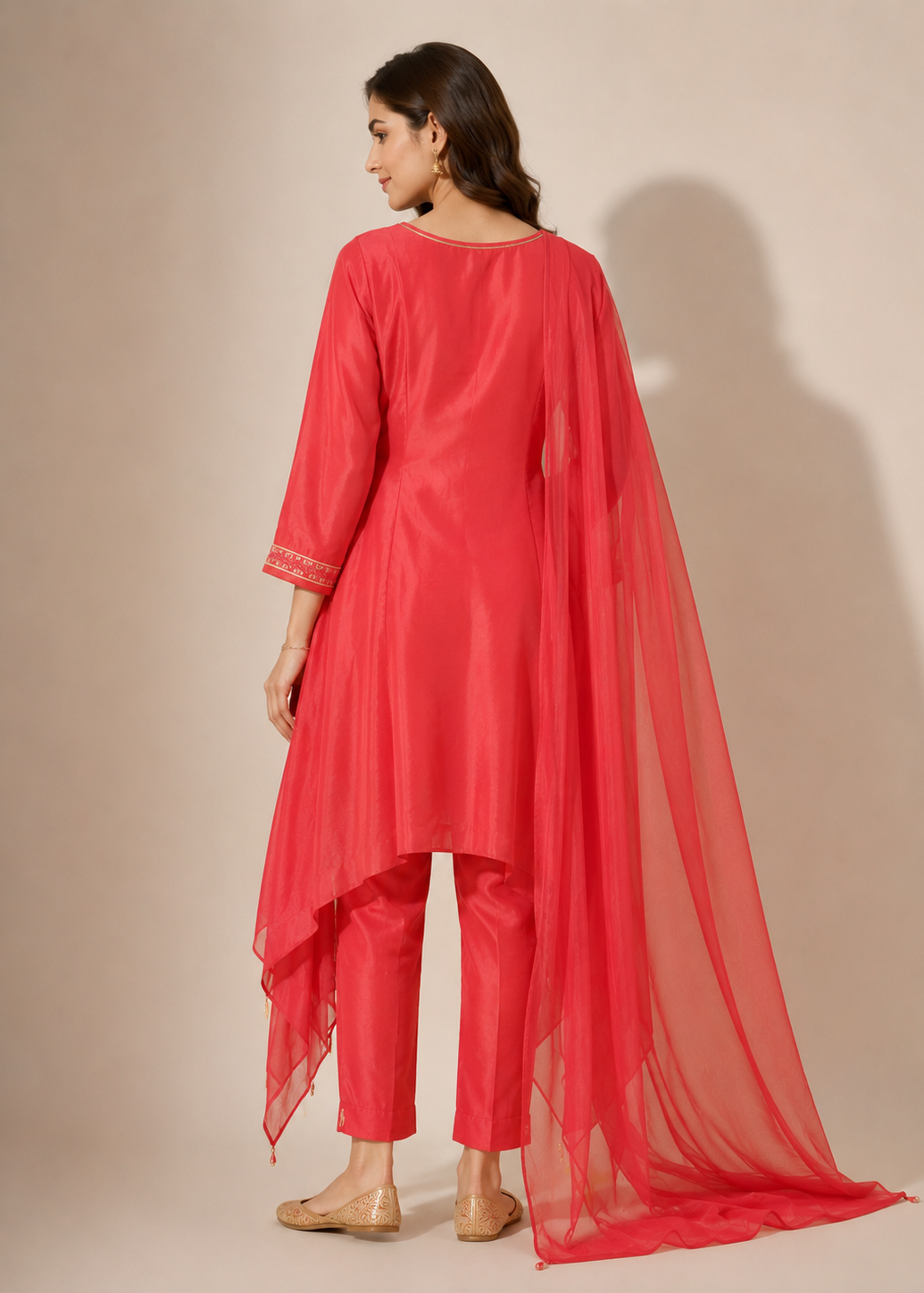 A woman modeling a bright red traditional outfit with a matching long sheer dupatta, shown from the back against a plain beige studio background.