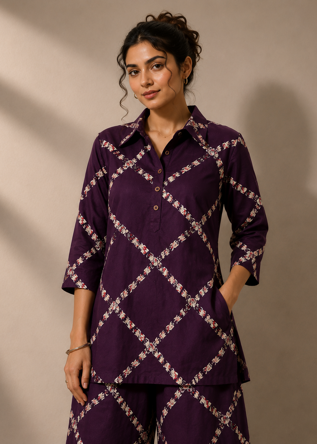 A woman modeling a matching purple two-piece set featuring a collared button-up shirt and trousers with a white and pink floral geometric lattice pattern, set against a neutral beige background.