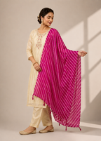 A woman modeling a traditional Indian outfit consisting of a cream-colored kurta and trousers, paired with a vibrant magenta pink dupatta featuring thin white stripes.