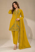 A woman modeling a mustard yellow ethnic three-piece suit set with green and gold embroidery, consisting of a long kurta, matching trousers, and a dupatta, set against a plain beige studio background.