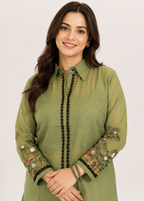 A woman wearing a sage green long-sleeve kurta with black beaded trim down the front and floral embroidery on the sleeves, set against a plain light background.