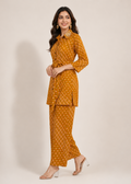 A woman modeling a mustard yellow two-piece kurta set with a white geometric pattern, featuring a long-sleeve button-up top and matching wide-leg pants, set against a plain beige studio background.