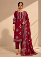 A woman models a deep maroon three-piece salwar kameez suit set with intricate silver and light blue embroidery, matching trousers, and a sheer dupatta with a paisley border, set against a warm beige background with soft shadows.