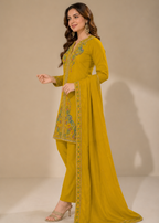 A woman modeling a mustard yellow traditional South Asian salwar kameez suit with floral embroidery on the kurta and matching dupatta, set against a plain beige studio background.