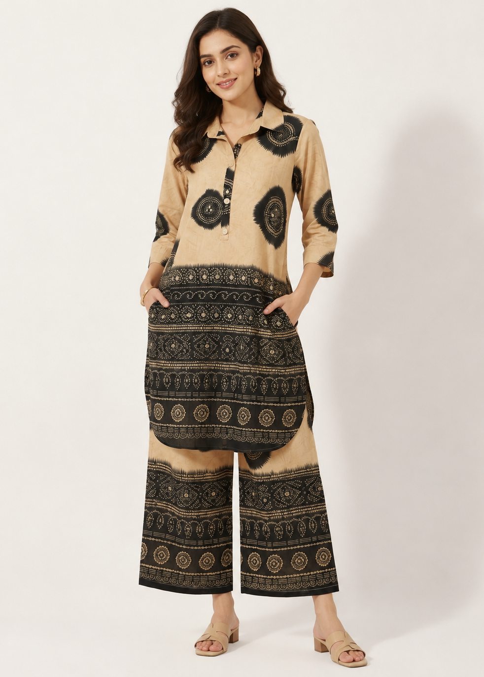 A woman modeling a beige and black printed two-piece kurta set with a collared long-sleeve top and wide-leg pants, standing against a plain light background.