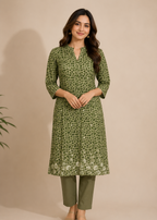 A woman modeling a green printed kurta with three-quarter sleeves and a split neckline, paired with olive green pants, against a solid beige studio background.