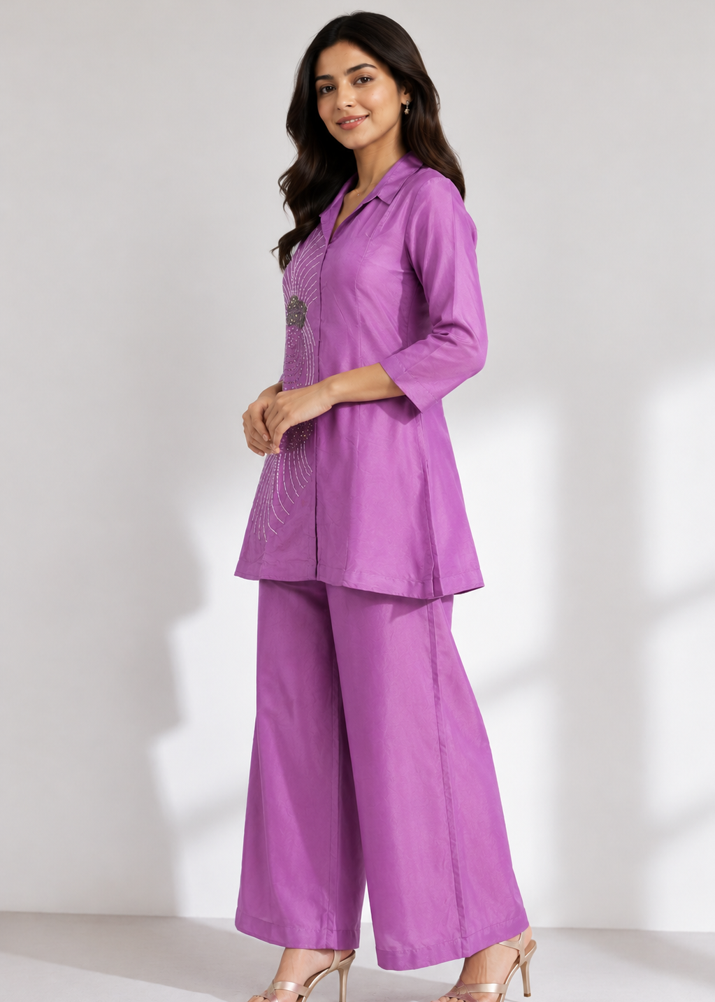 A woman modeling a purple two-piece kurta set with wide-leg pants and three-quarter sleeves, standing against a light gray studio background.