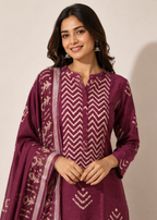 A woman modeling a traditional Indian outfit consisting of a deep purple kurta with cream chevron patterns, a matching dupatta, and silver earrings, set against a plain beige background.