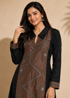 A woman modeling a brown and black kurta with metallic embroidered details, set against a warm beige background with a soft palm shadow.