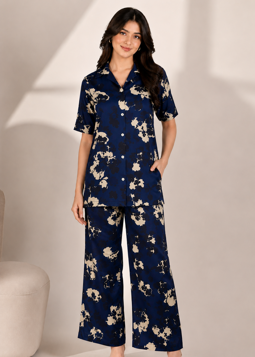 A woman modeling a matching two-piece pajama set with a navy blue base and beige floral print, featuring a short-sleeve button-up top and wide-leg pants.