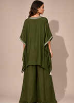 A woman modeling an olive green two-piece kurta set, shown from the back against a solid beige studio background.