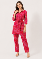 A woman modeling a red three-piece matching set featuring a collared long-sleeve top with a tie waist, matching cropped pants, and a pattern of white dots and diagonal stripes, set against a plain light gray background.