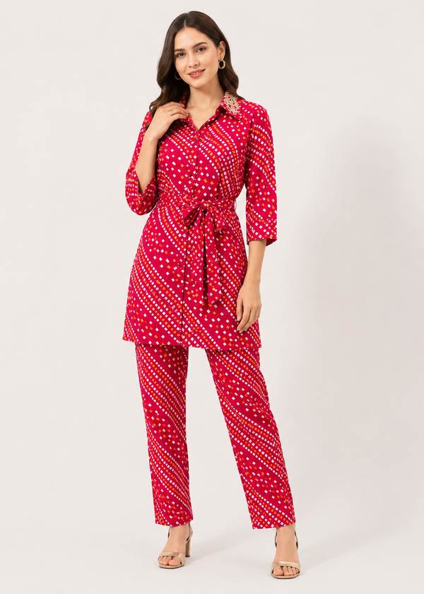 A woman modeling a red three-piece matching set featuring a collared long-sleeve top with a tie waist, matching cropped pants, and a pattern of white dots and diagonal stripes, set against a plain light gray background.