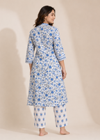 A woman modeling a white three-piece kurta set with blue floral block prints, shown from the back against a warm beige studio backdrop.