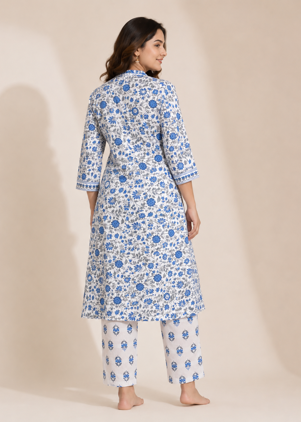 A woman modeling a white three-piece kurta set with blue floral block prints, shown from the back against a warm beige studio backdrop.
