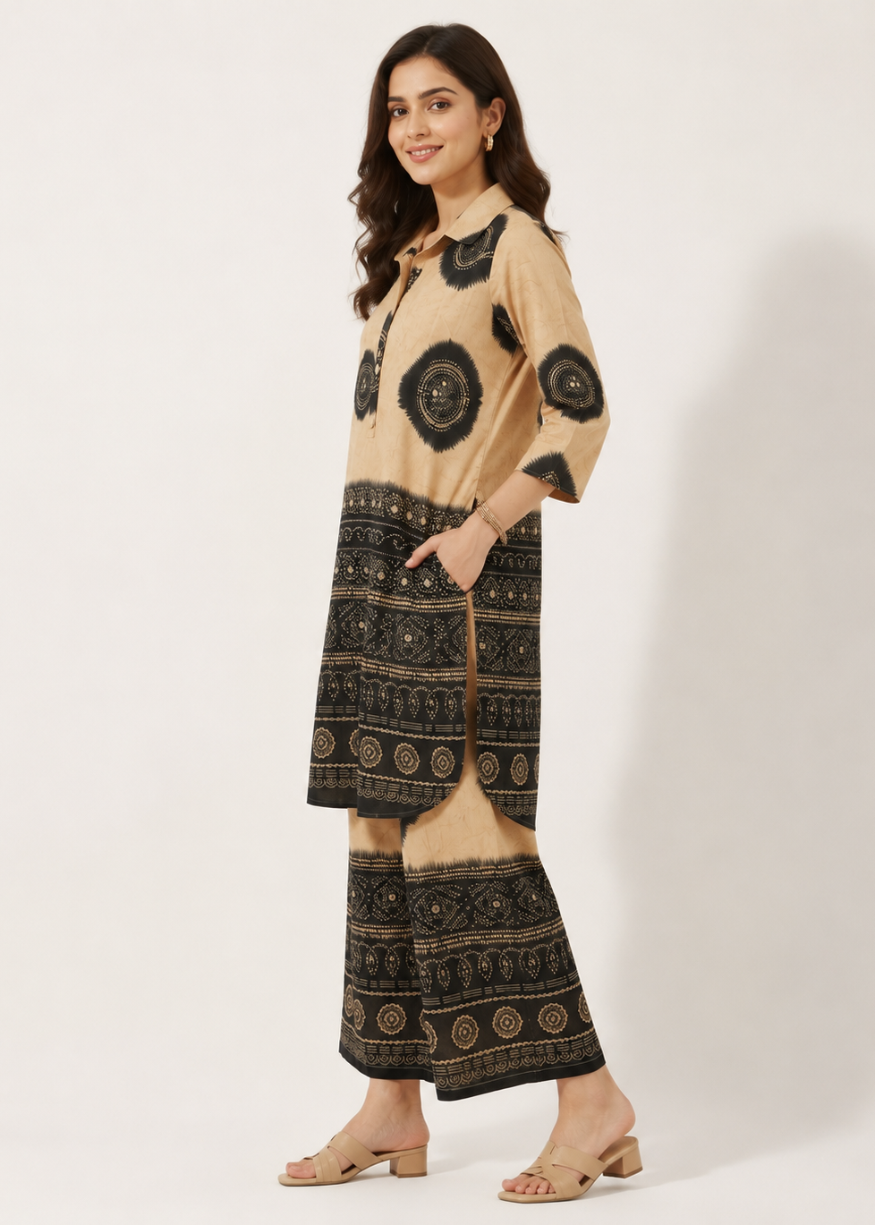 A woman modeling a beige and black printed kurta set with matching wide-leg pants, standing against a plain off-white studio background.