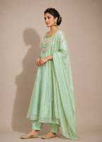 A woman modeling a mint green traditional Indian outfit with a matching dupatta, set against a solid beige studio background.