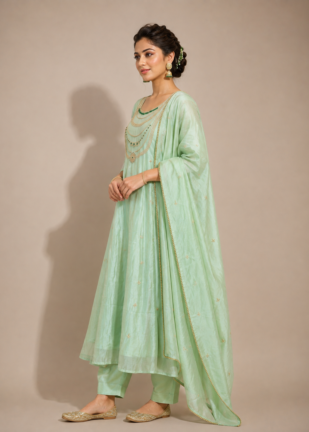 A woman modeling a mint green traditional Indian outfit with a matching dupatta, set against a solid beige studio background.