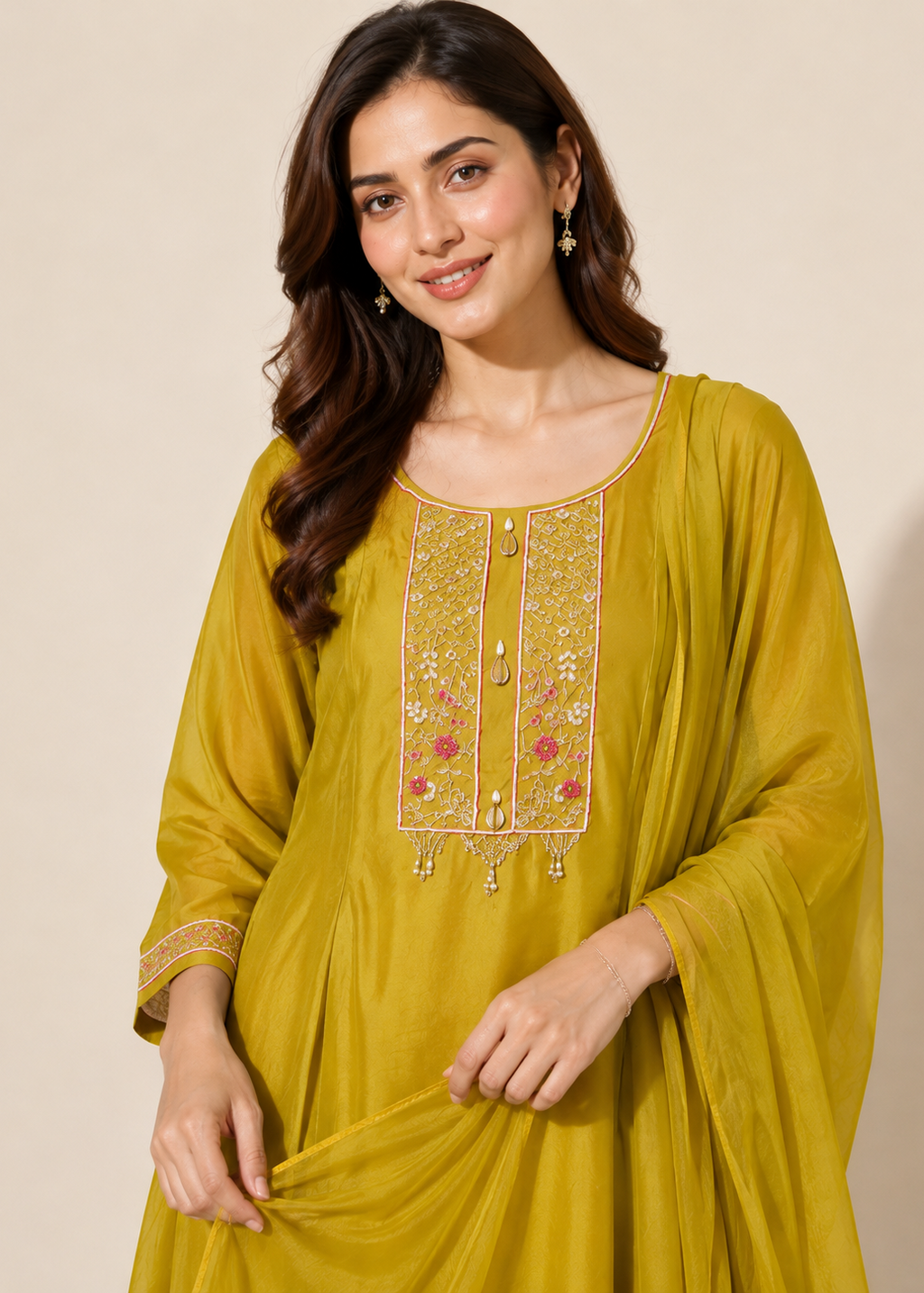 A woman wearing a mustard yellow traditional Indian kurta with gold and pink floral embroidery on the chest, set against a plain beige background.