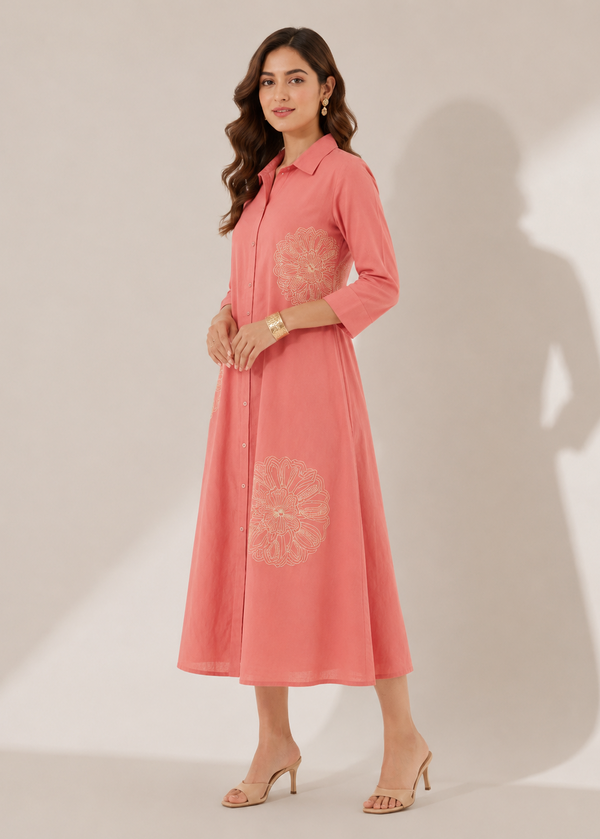 A woman models a pink collared midi dress with three-quarter sleeves and light beige floral embroidery on the bodice and skirt, standing against a neutral beige studio background with soft shadows.