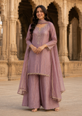 A woman models a lavender purple traditional Indian outfit with matching dupatta and wide-leg pants, standing in front of an ornate stone archway.