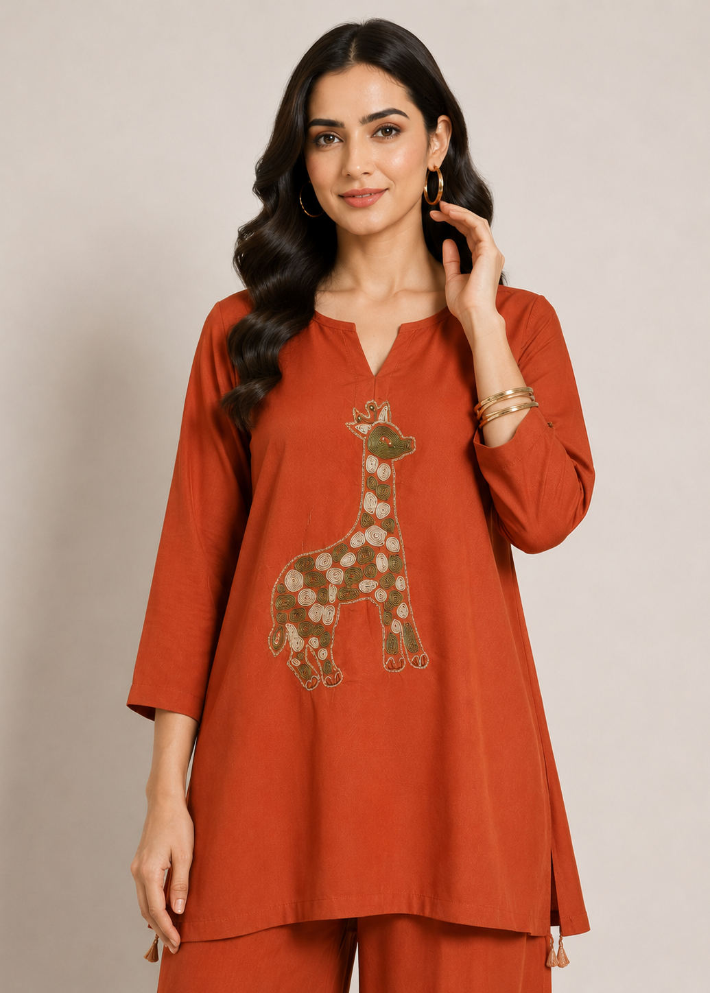 A woman modeling a rust-orange cotton kurta with a giraffe patchwork design on the front, paired with matching rust-orange trousers, set against a plain beige studio background.