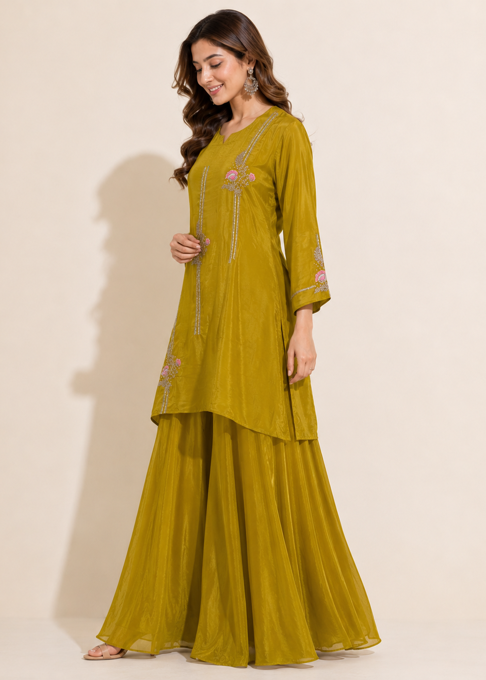 A woman modeling a three-piece olive green traditional Indian outfit with a tunic, flared pants, and embroidered details, set against a plain beige studio background.