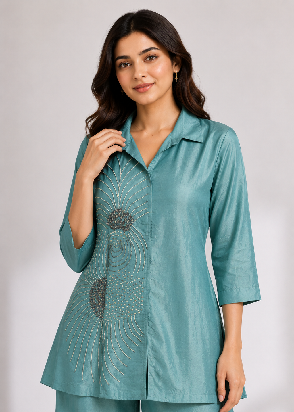 A woman modeling a teal blue-green satin kurta with gold embroidered sunburst patterns on the front, paired with matching trousers, against a light gray studio background.