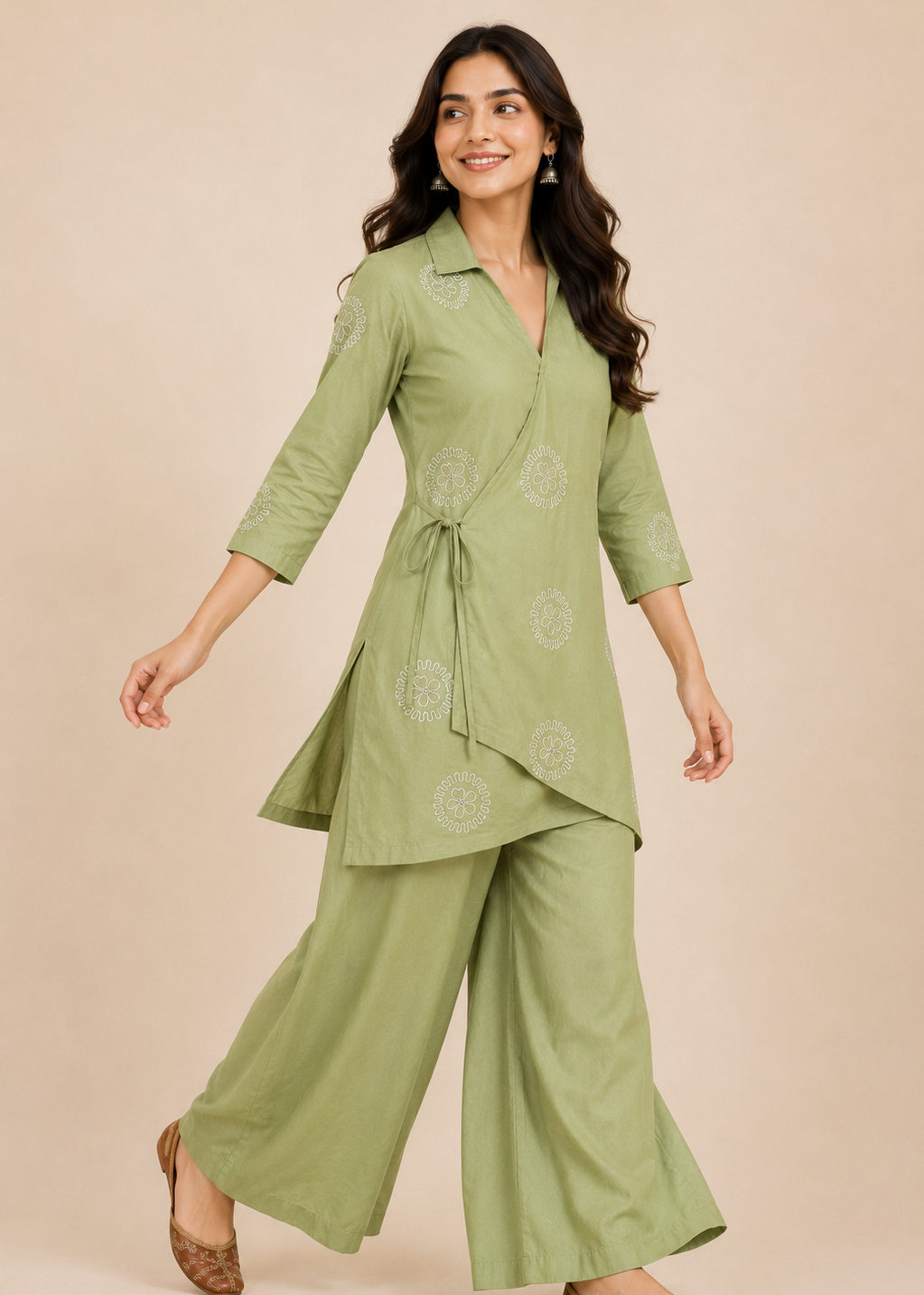 A woman modeling a sage green two-piece kurta set with matching wide-leg pants, featuring light embroidery and a tie waist, set against a solid beige background.