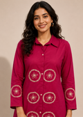 A woman wearing a magenta button-up kurta with white floral embroidery on the front and cuffs, set against a plain beige background.