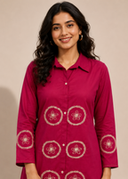 A woman wearing a magenta button-up kurta with white floral embroidery on the front and cuffs, set against a plain beige background.