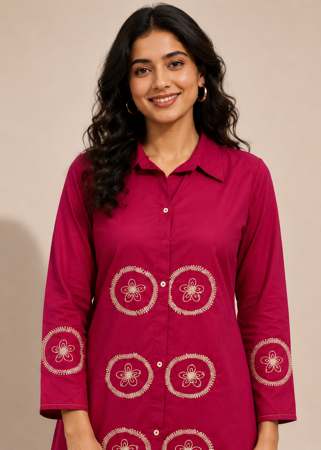 A woman wearing a magenta button-up kurta with white floral embroidery on the front and cuffs, set against a plain beige background.
