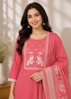 A woman modeling a pink Indian ethnic salwar kameez suit with white printed elephant motifs on the chest and a matching printed dupatta, set against a warm beige background with soft window shadows.