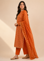 A woman modeling an orange traditional outfit with intricate embroidery on the kurta, matching orange pants, and a striped orange dupatta, set against a warm beige background.