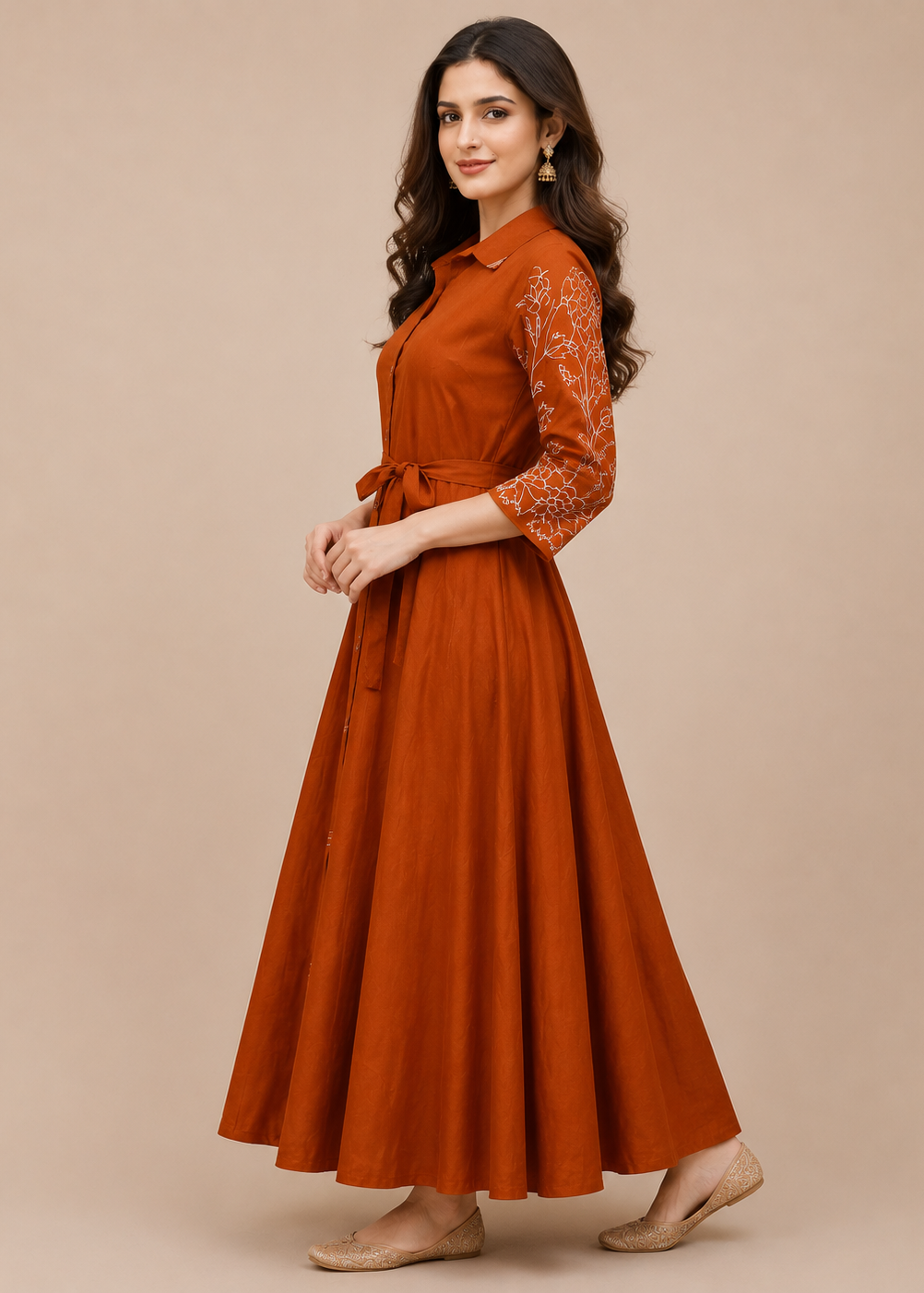 A woman modeling a rust-orange maxi dress with three-quarter sleeves featuring white floral embroidery, set against a solid beige studio background.