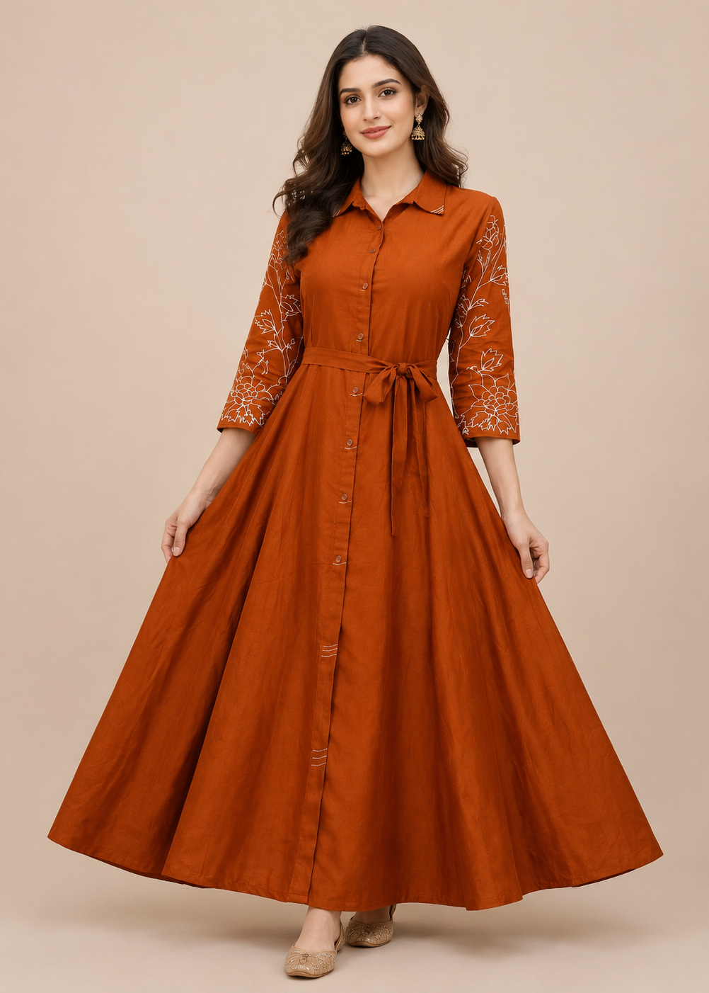 A woman modeling a rust-orange maxi shirt dress with white floral embroidery on the three-quarter sleeves, set against a solid beige studio background.