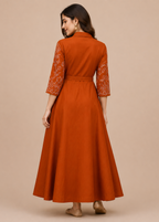 A woman wearing a rust-orange maxi dress with lace sleeves, shown from the back against a solid beige studio background.