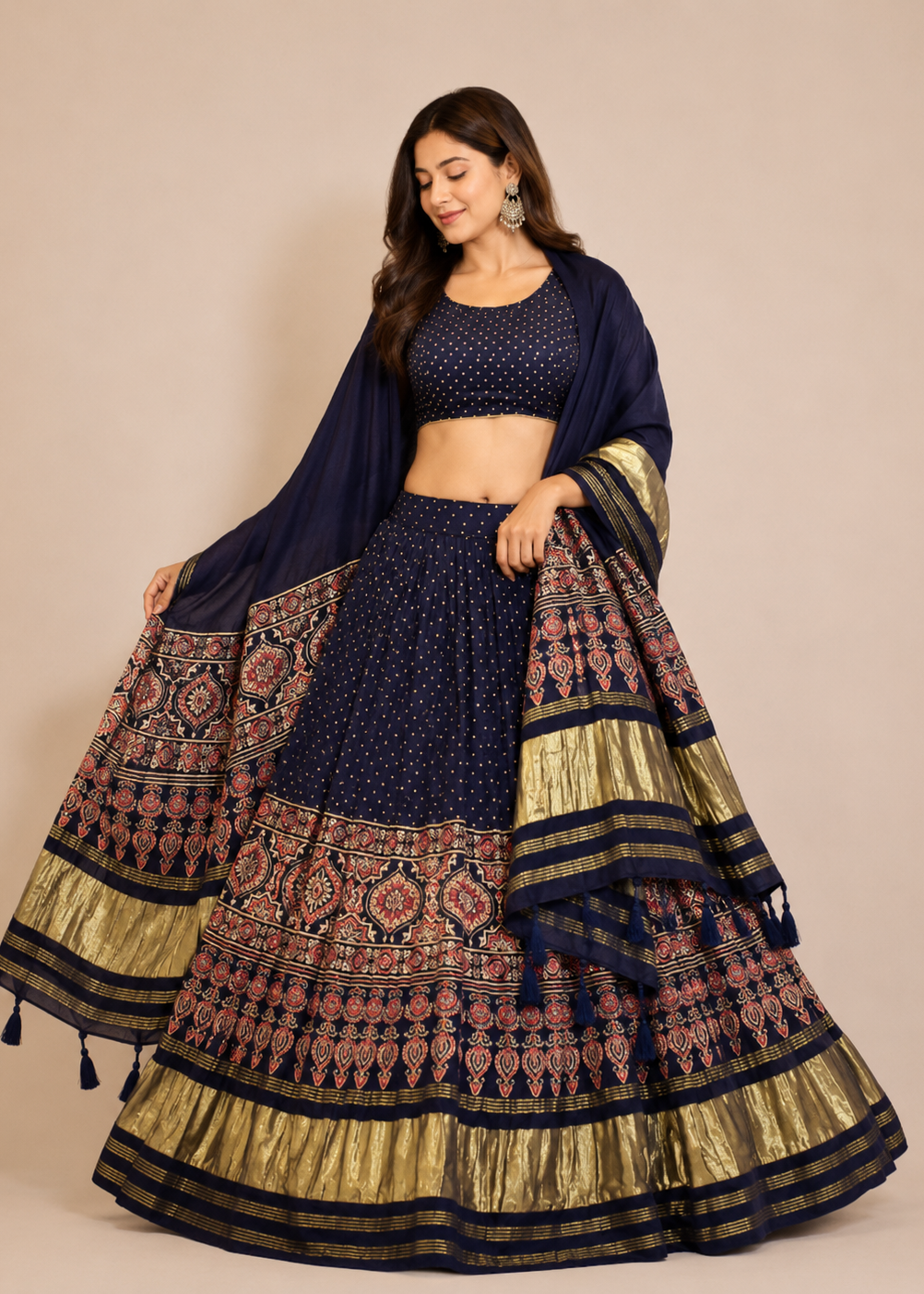 A woman models a navy blue and gold embroidered Indian ethnic lehenga choli set against a solid beige studio background.